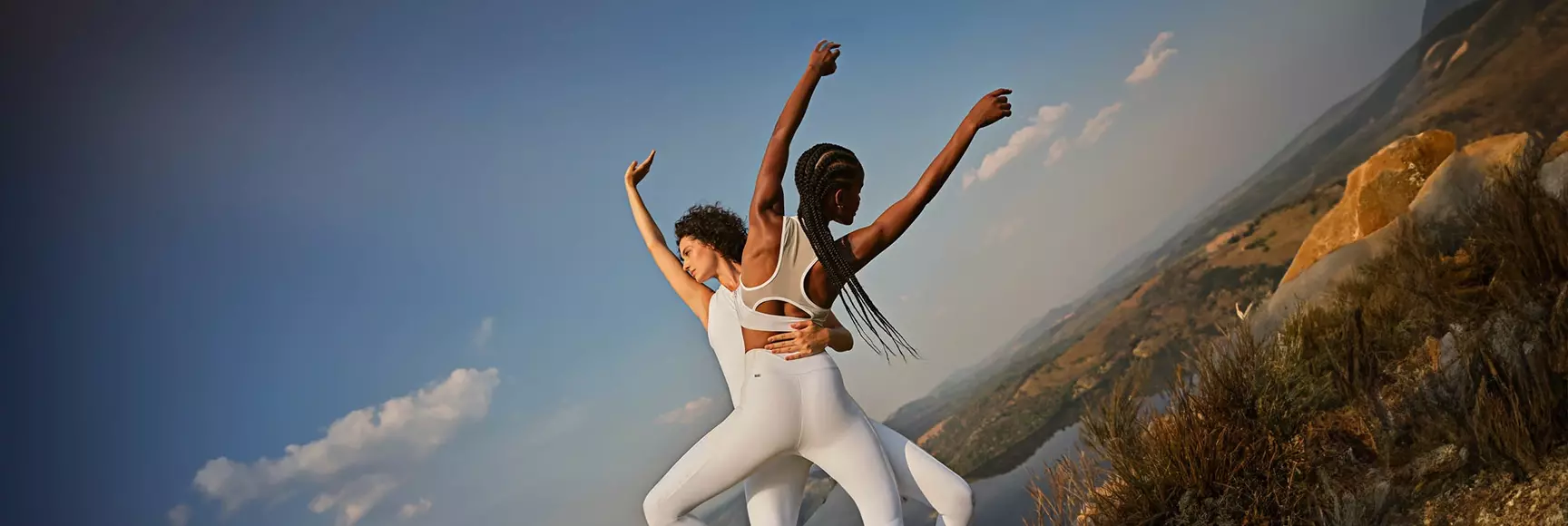 Two people stretch on a mountaintop in white activewear.