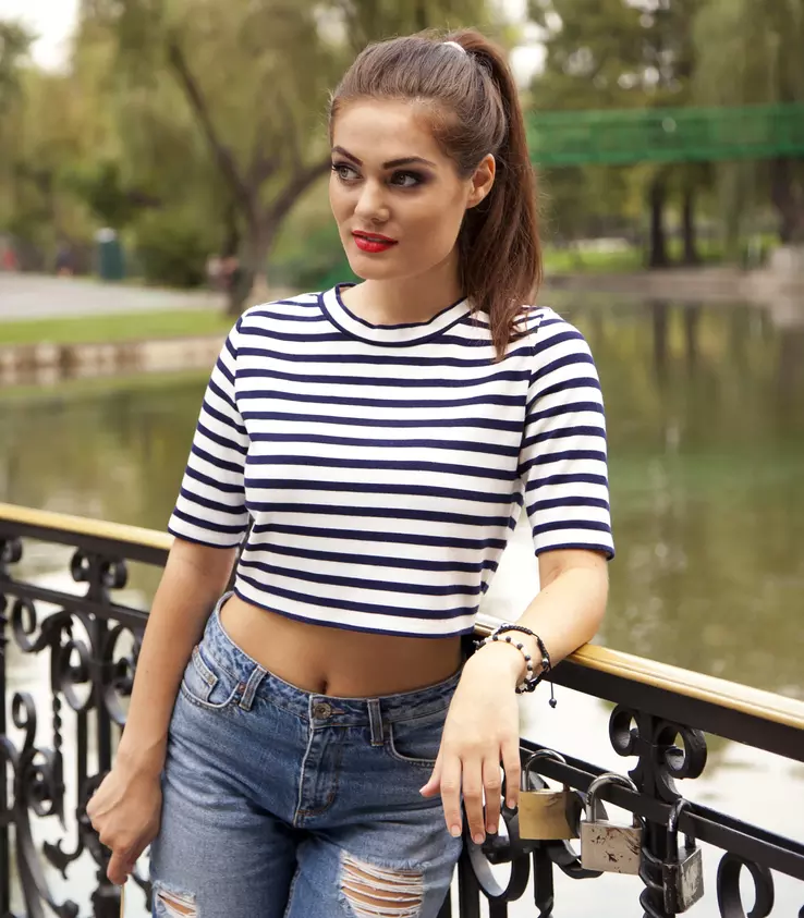 A woman wears ripped jeans and a crop top that exposes her midriff—a popular fashion of the first years of the 21st century.